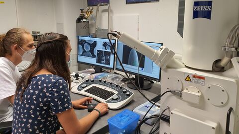 Zwei Schüler sitzen vor Tastatur, Bildschirm und Mikroskop