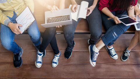 Mehrere Personen auf einer Bank mit Laptops und Tablets