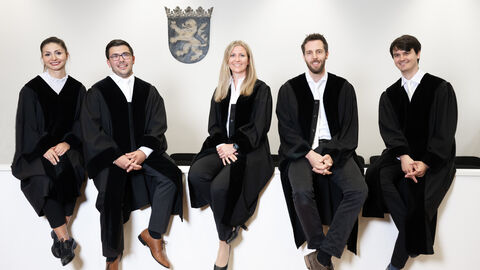 Fünf Juristinnen und Juristen sitzen auf einer Richterbank vor dem Hessenwappen