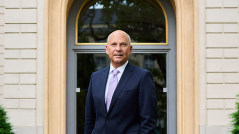 Portrait von Justizminister Prof. Dr. Roman Poseck vor der Eingangstür zu einem Gebäude