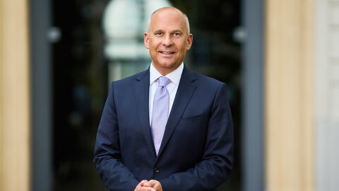 Portrait von Justizminister Prof. Dr. Roman Poseck vor der Eingangstür zu einem Gebäude