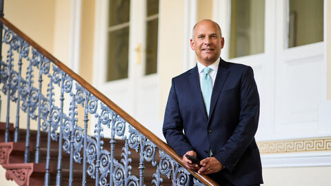 Portrait von Justizminister Prof. Dr. Roman Poseck auf einer Treppe, an das Geländer gelehnt.