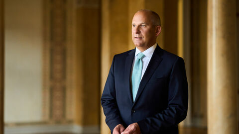 Portrait von Justizminister Prof. Dr. Roman Poseck in einem Saal mit Bögen im Hintergrund