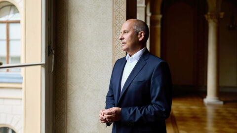 Portrait von Justizminister Prof. Dr. Roman Poseck in einem Saal mit Bögen im Hintergrund, er schaut aus einem Fenster
