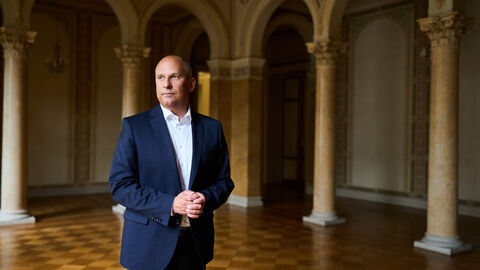 Portrait von Justizminister Prof. Dr. Roman Poseck in einem Saal mit Bögen im Hintergrund