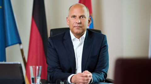 Portrait von Justizminister Prof. Dr. Roman Poseck sitzend an einem Tisch.