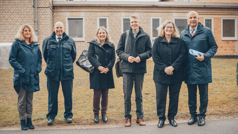 Justizminister Poseck gemeinsam mit mehreren Beteiligten in der JVA Frankfurt IV. Sie stehen aufgereiht am Straßenrand und lächeln in die Kamera, im Hintergrund ein Justizgebäude.