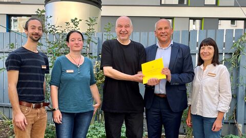 Justizminister Poseck mit Beteiligten der Sozialen Hilfe Kassel. Sie stehen nebeneinander vor einem Gebäude mit dem Zuwendungsbescheid in Händen.