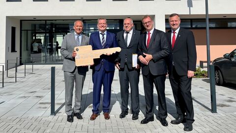 Justizminister Prof. Dr. Roman Poseck mit weiteren Beteiligten vor dem neuen Gebäude. Sie stehen nebeneinander und halten einen überdimensional großen Schlüssel in Händen.