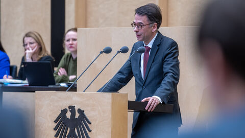 Christian Heinz im Bundesrat Christian Heinz steht am Rednerpult im Bundesrat. Er lehnt sich auf das Pult und spricht in zwei Mikrofone. Auf der Front des Pults ist der Bundesadler zu sehen.