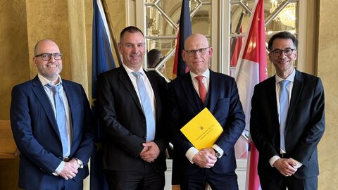 Vizepräsident des Amtsgerichts Gießen Dr. Dietrich Becker, Präsident des Oberlandesgerichts Frankfurt am Main Dr. Alexander Seitz, Präsident a.D. des Amtsgerichts Gießen Meinrad Wösthoff und Justizminister Christian Heinz stehen nebeneinander zum Foto aufgestellt. Im Hintergrund sind Flaggen zu sehen.