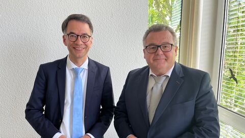 Justizminister Heinz steht neben einem weiteren Mann, sie lächeln beide in die Kamera.