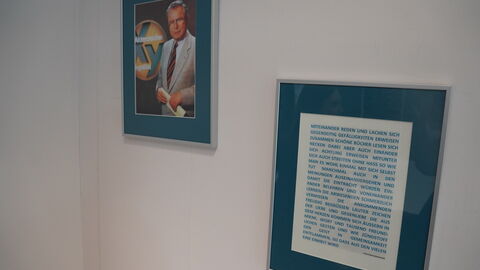 Zwei Bilder, eines mit viel Text hängen an einer weißen Wand. Das zweite ist ein älteres Bild mit einem Mann und dem Schriftzug "Aktenzeichen XY ungelöst" darauf.