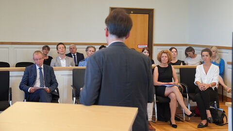 Justizminister Heinz bei dem Amtsgericht Wetzlar Justizminister Heinz steht vor Personen in einem Raum und spricht zu ihnen. Die Personen sitzen und sind ihm zugewandt.