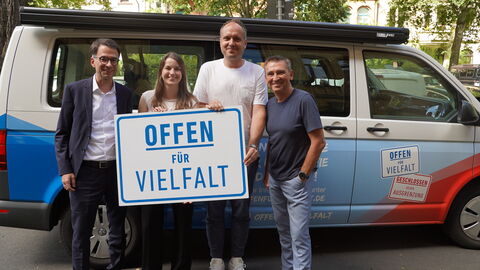 Initiative Offen für Vielfalt Justizminister Heinz steht mit weiteren Personen vor einem Fahrzeug. Sie halten ein Schild mit der Aufschrift "Offen für Vielfalt" vor sich.