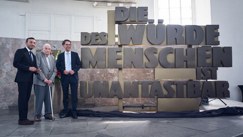 Herr Oberbürgermeister Josef, Herr Wiese und Herr Justizminister Christian Heinz neben Denkmal Herr Oberbürgermeister Josef, Herr Wiese und Herr Justizminister Christian Heinz stehen neben Denkmal mit Schriftzug: "Die Würde des Menschen ist unantastabar"