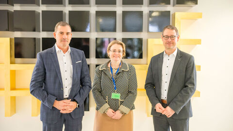 Zwei Männer und eine Frau stehen vor einer Wand.