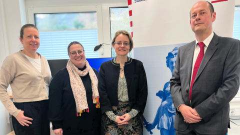 Justizstaatssekretärin Tanja Eichner steht mit weiteren Personen zum Gruppenfoto aufgestellt vor einem Aufsteller mit der Aufschrift "Staatsanwaltschaft Marburg".