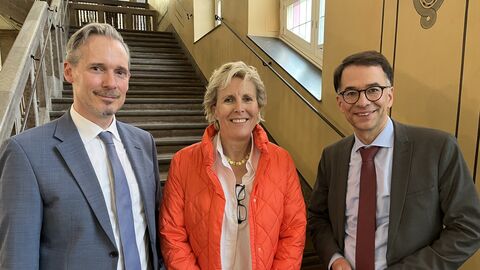 Zwei Männer und eine Frau stehen vor einer Treppe.