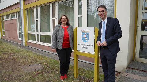 Präsidentin des Verwaltungsgerichts Gießen Sabine Dörr und Justizminister Christian Heinz Eine Frau und ein Mann stehen jeweils neben einem Gebäudeschild mit der Aufschrift "Verwaltungsgericht Gießen"