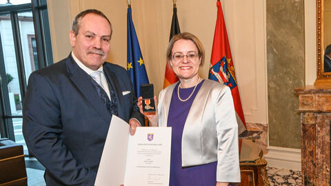Tanja Eichner hält eine Medaille in ihrer Hand und steht neben Jürgen Michel der ein Zertifikat präsentiert - beide sind festlich gekleidet.