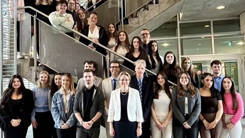 Justizstaatssekretärin Tanja Eichner steht mit den Anwärterinnen und Anwärtern auf einer Treppe zum Gruppenfoto aufgestellt.