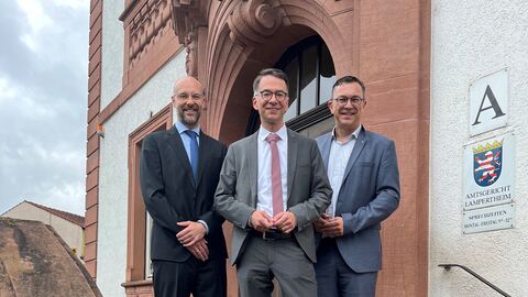 Drei Mäner stehen auf einer Treppe vor einem Gebäude.