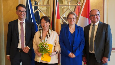 Christina Kreis hält einen Blumenstrauß und eine Urkunde in den Händen, an ihrer Seite Justizminister Heinz und zwei weitere Personen