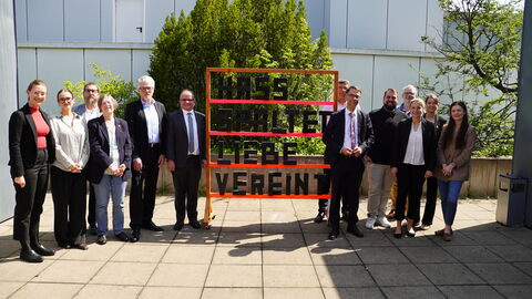 Dreizehn Menschen stehen draußen. In der Mitte steht ein aus Holz gebautes Gestell mit der Schrift "Hass spaltet, Liebe vereint"