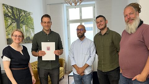 Fünf Personen stehen nebeneinander. Eine Person hält ein Dokument hoch.