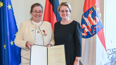 Zwei Frauen stehen vor der Europa, Deutschland und der Hessenflagge und halten Auszeichnung in den Händen.