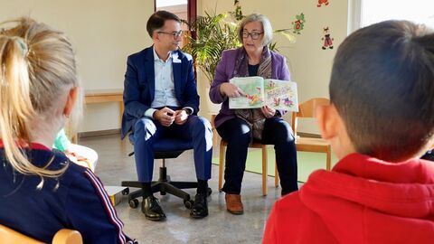 Zwei Personen zeigen Kindern ein Buch.