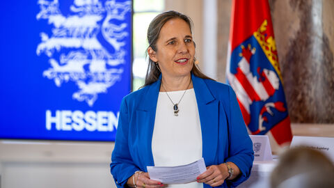 Eine Frau hält einen Zettel in der Hand und schaut leicht nach links.